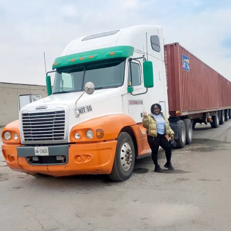 Smiling woman giving a peace sign beside a white and orange semi-truck hauling a red shipping container