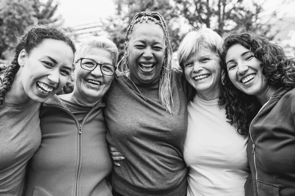 Five women of different ages laughing with their arms around each other